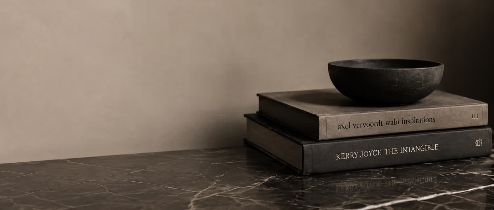 A dark carved bowl resting on design books on a marble surface