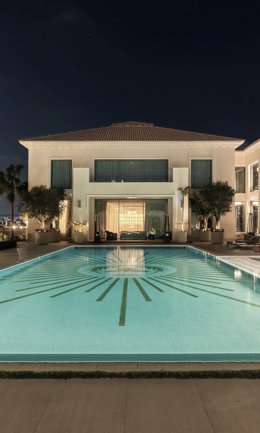 A villa exterior at dusk, the pool and planting lit from within the garden